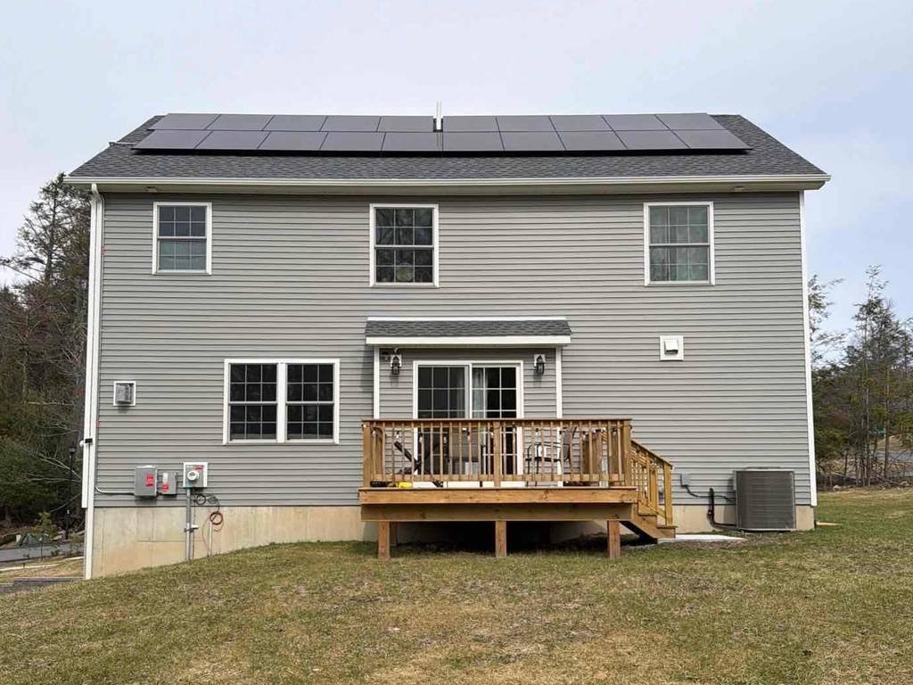 Back of a gray colonial with solar panels above a new deck