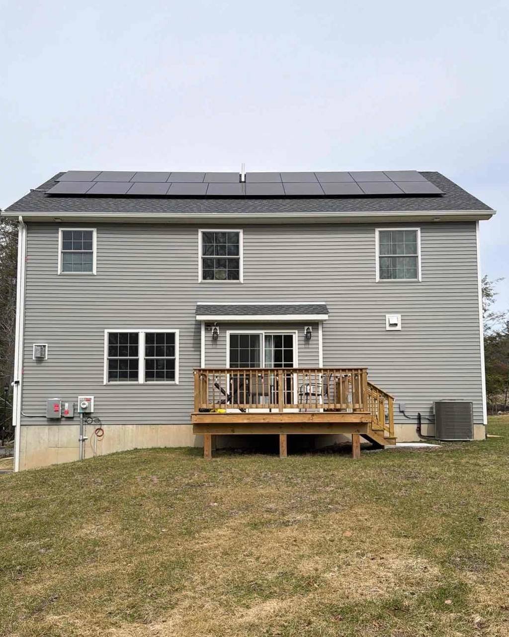 Back of a gray colonial with solar panels above a new deck