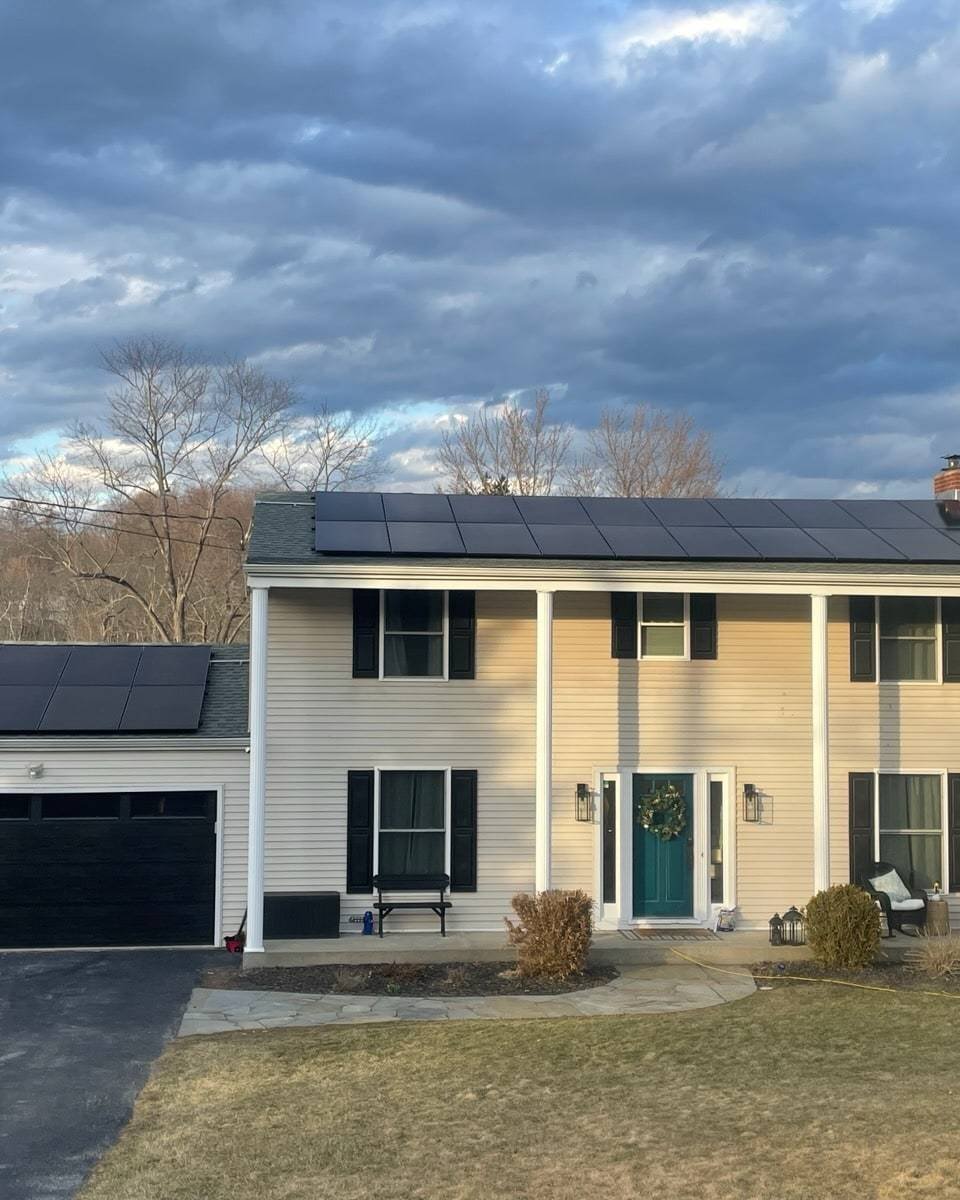 White colonial home with solar panels on the main roof and attached garage